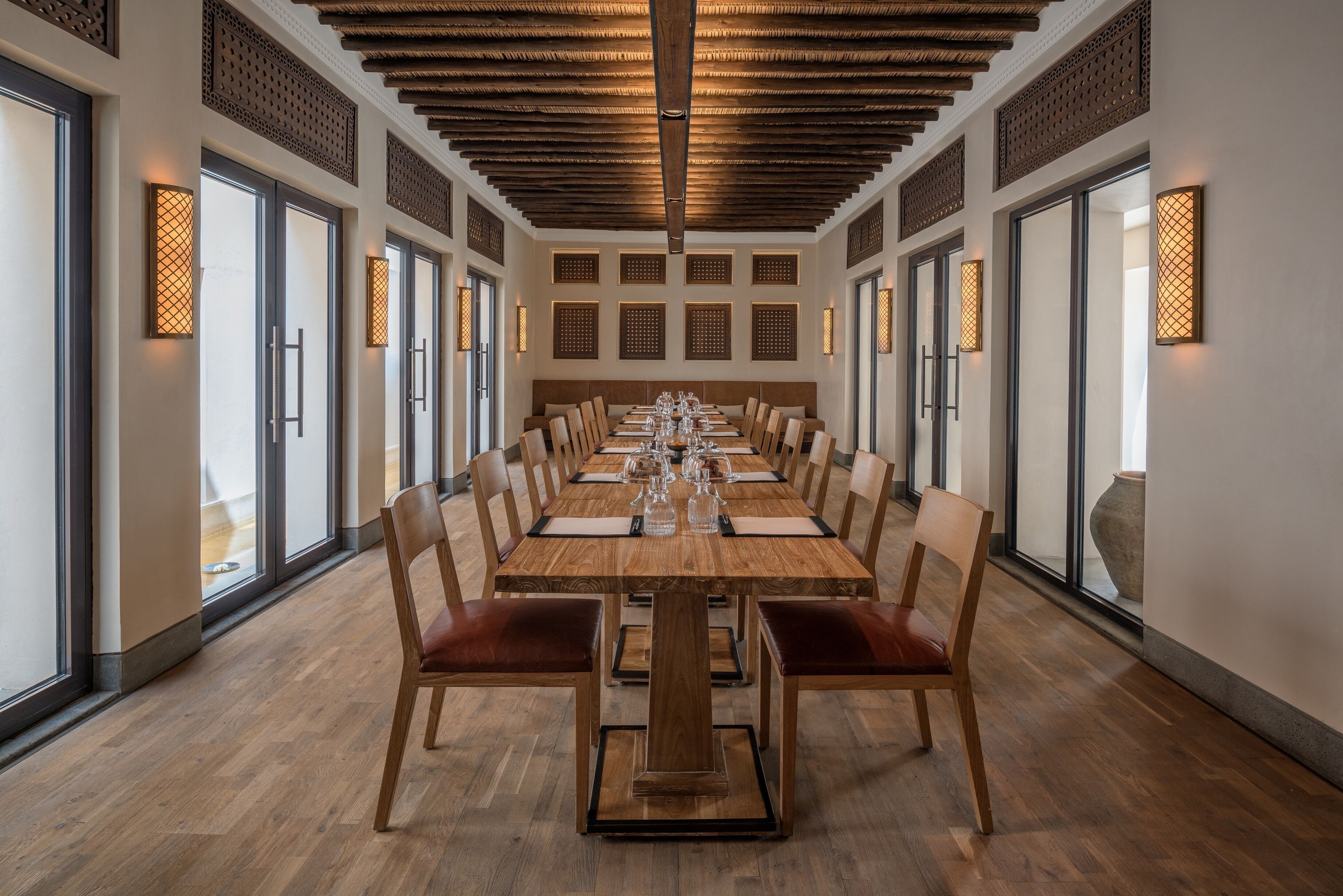 A long dining table with chairs, wooden flooring, and decorative wall panels.
