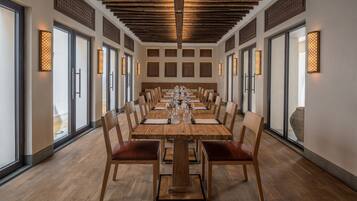 A long dining table with chairs, wooden flooring, and decorative wall panels.