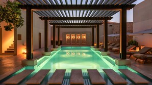 A pool area with a pergola, lounge chairs, and a stone wall with lights. - The Chedi Al Bait, Sharjah, UAE (Sharjah)