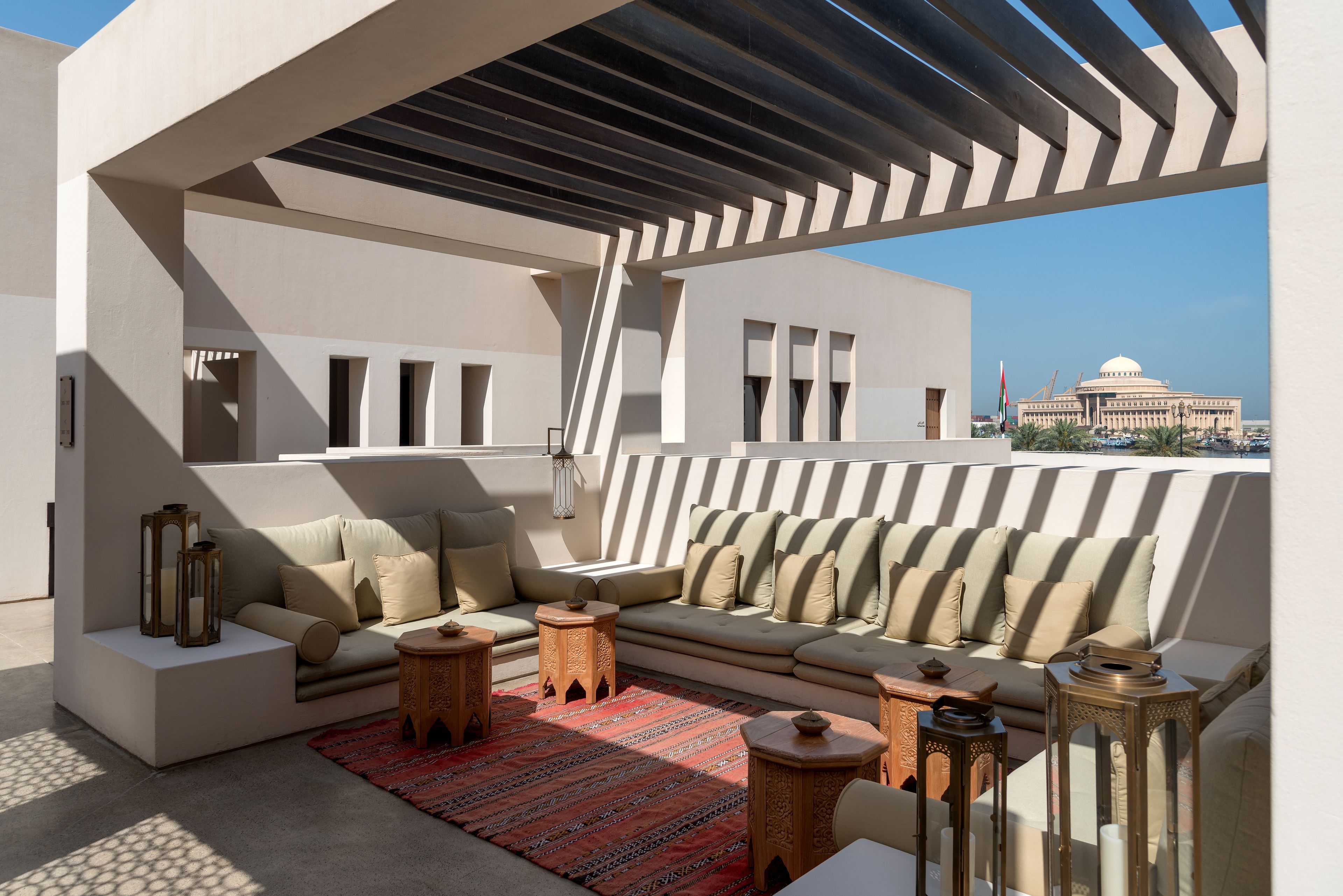 Un área de estar moderna al aire libre con un sofá y cojines, un tapete estampado y faroles decorativos.