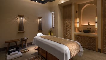 Un cuarto de spa con una camilla de masaje, un banco de madera y una pequeña mesa con toallas y un tazón.