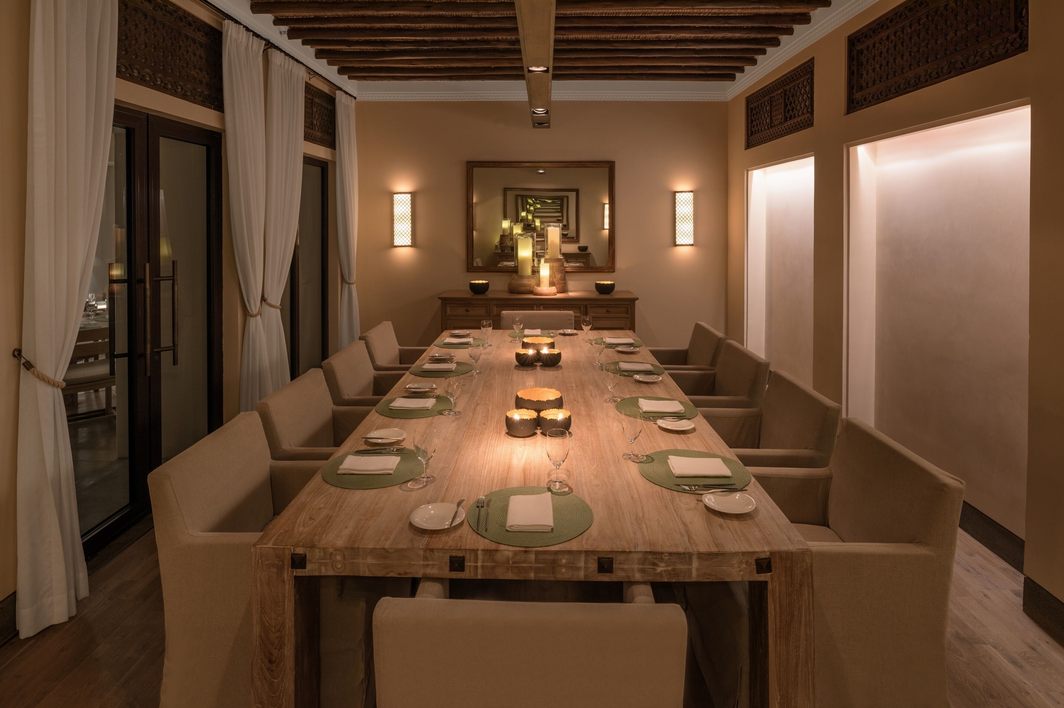 A long dining table with chairs, candles, and a mirror on the wall.