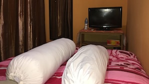 A hotel room with a bed, a television on a stand, a water bottle, and a door with stickers.