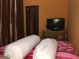 Una habitación de hotel con una cama, un televisor sobre un mueble, una botella de agua y una puerta con pegatinas.