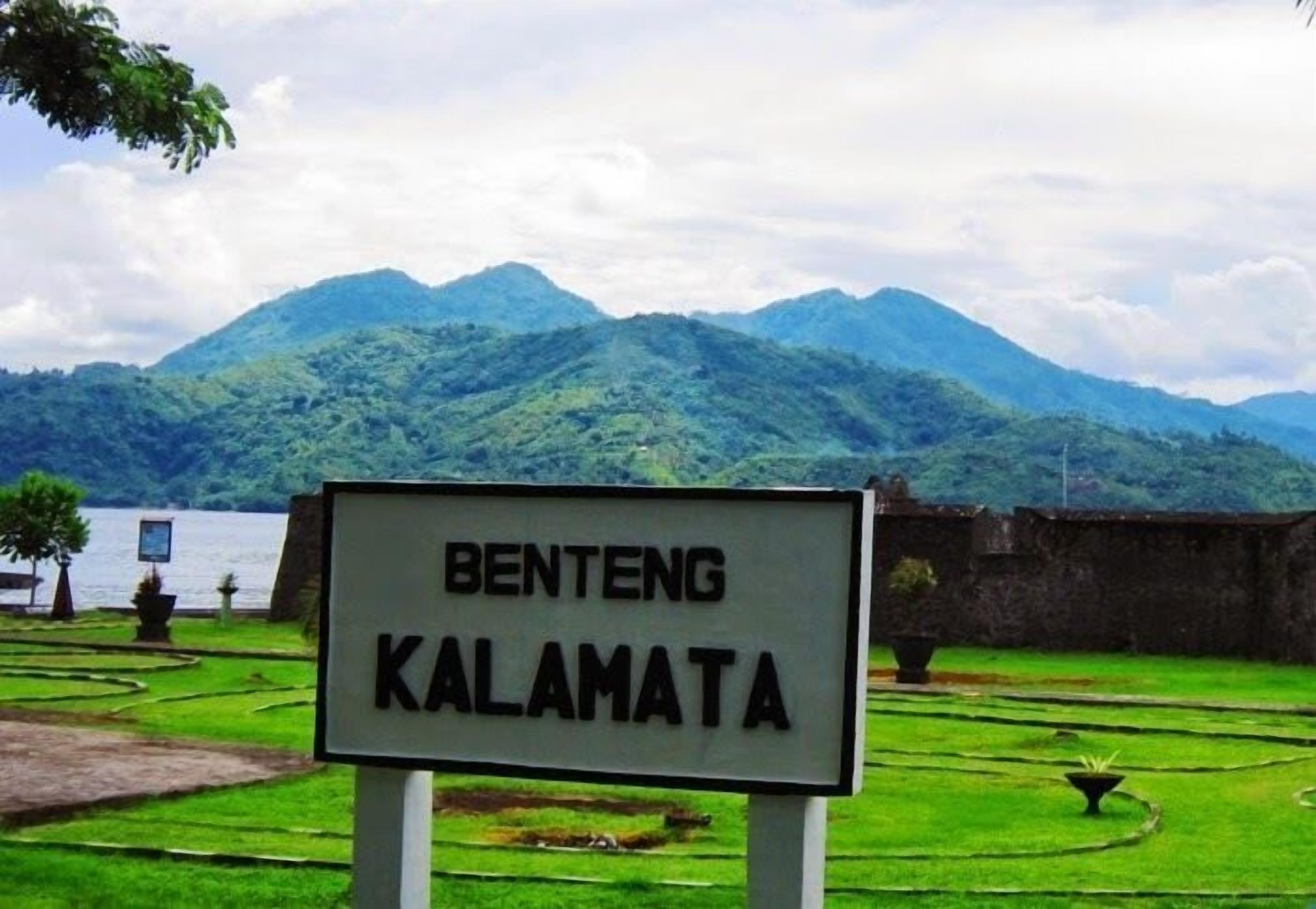 A sign reading "BENTENG KALAMATA" in a lush green landscape with mountains in the background.