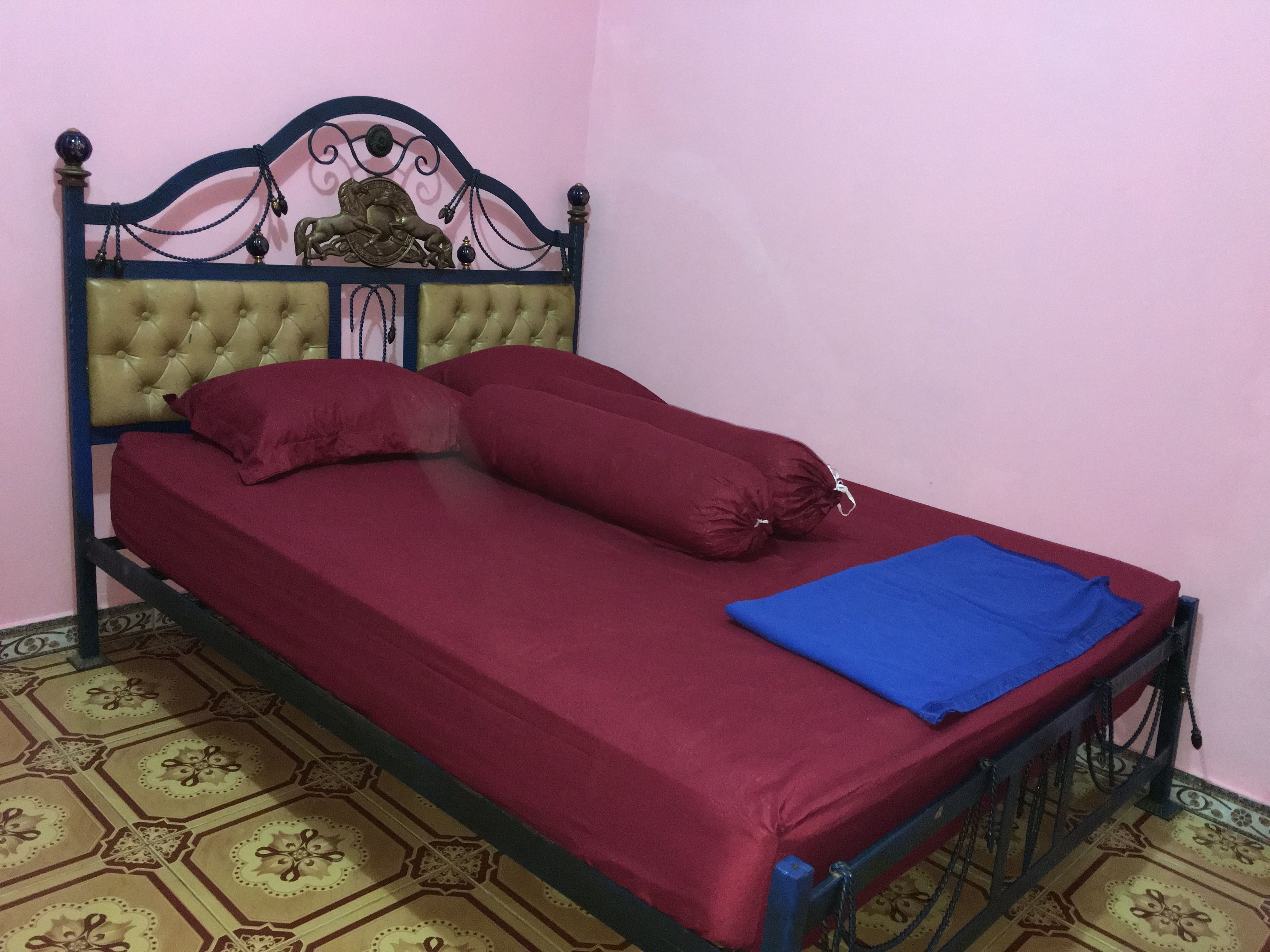 A single bed with a headboard, red bedding, and a blue blanket.