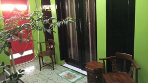 A room with a green wall, a tiled floor, a wooden chair, a small table, and a potted plant.