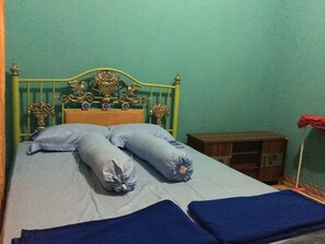 Un lit avec un cadre en métal vert, une tête de lit en bois et un matelas bleu. Il y a des oreillers et une couverture sur le lit.