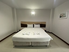 Una cama doble bien tendida con cabecera, una mesita de noche y un aplique de pared.