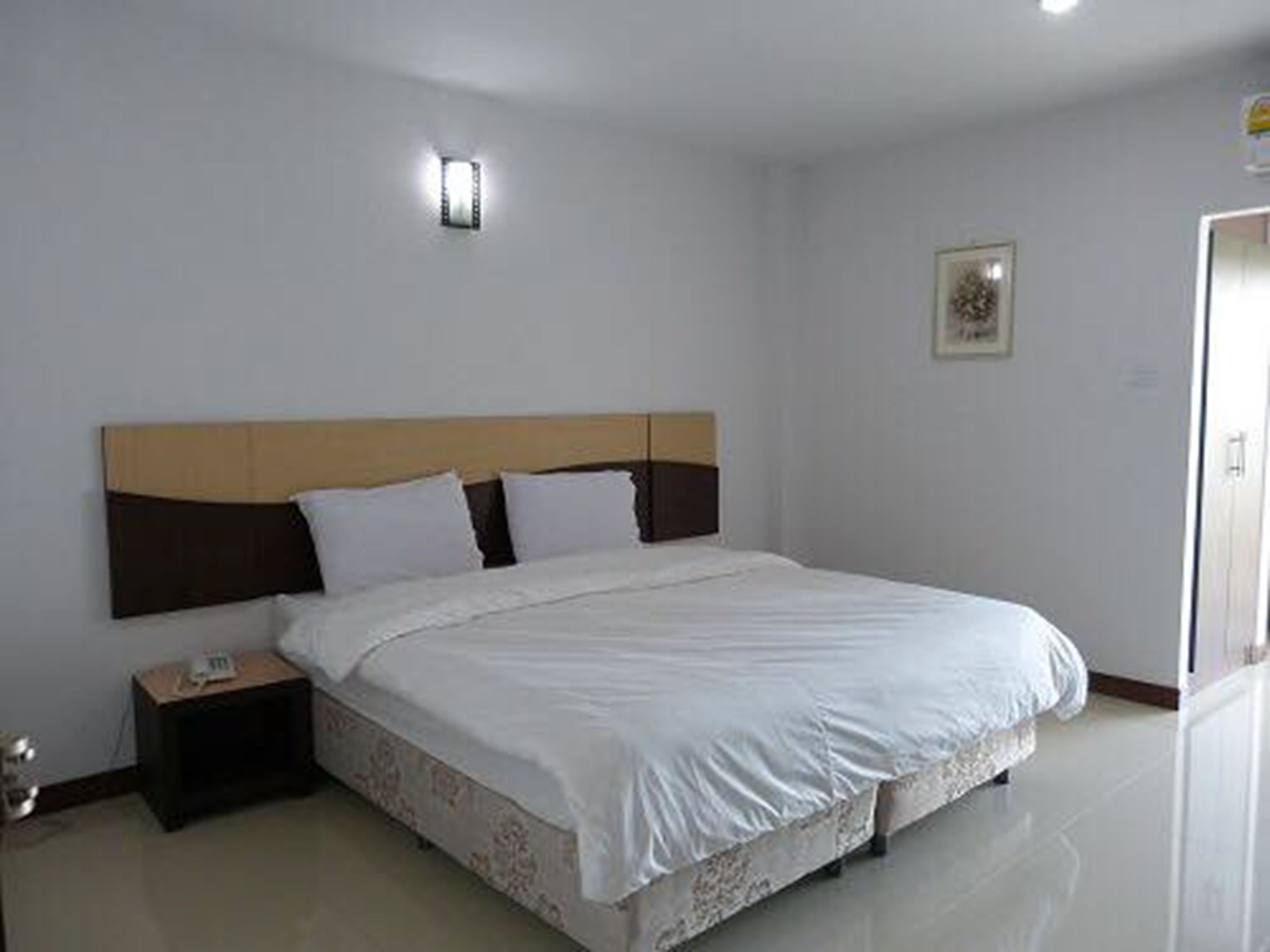 A neatly made bed with white linens, a wooden headboard, and a bedside table with a lamp.