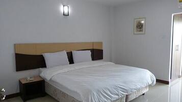 A neatly made bed with white linens, a wooden headboard, and a bedside table with a lamp.