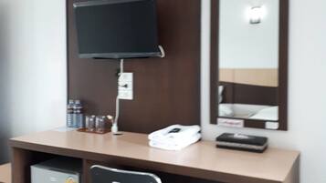 Habitación de hotel con escritorio de madera, televisor de pantalla plana, espejo, refrigerador pequeño y una silla.