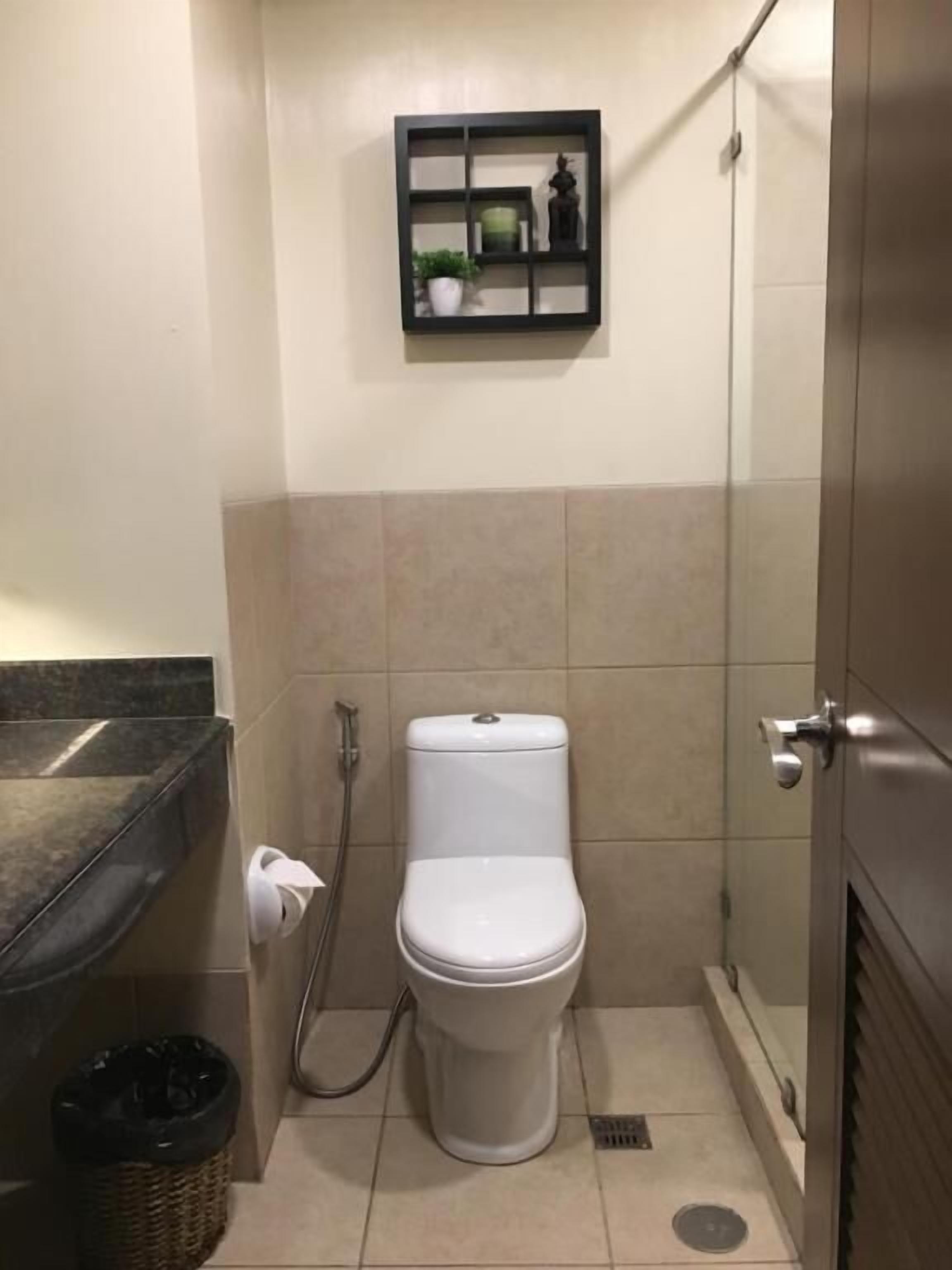Une petite salle de bain comprenant des toilettes, une petite étagère au-dessus, une poubelle et un espace douche.