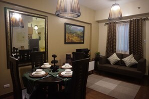 A dining area with a table set for four, a sofa with patterned cushions, and a painting on the wall.