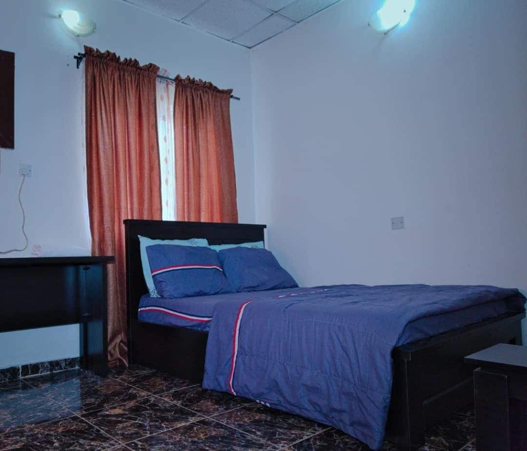 A bedroom with a bed, a nightstand, a dresser, and a window with curtains.