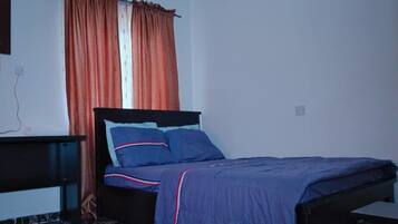 A bedroom with a bed, a nightstand, a dresser, and a window with curtains.