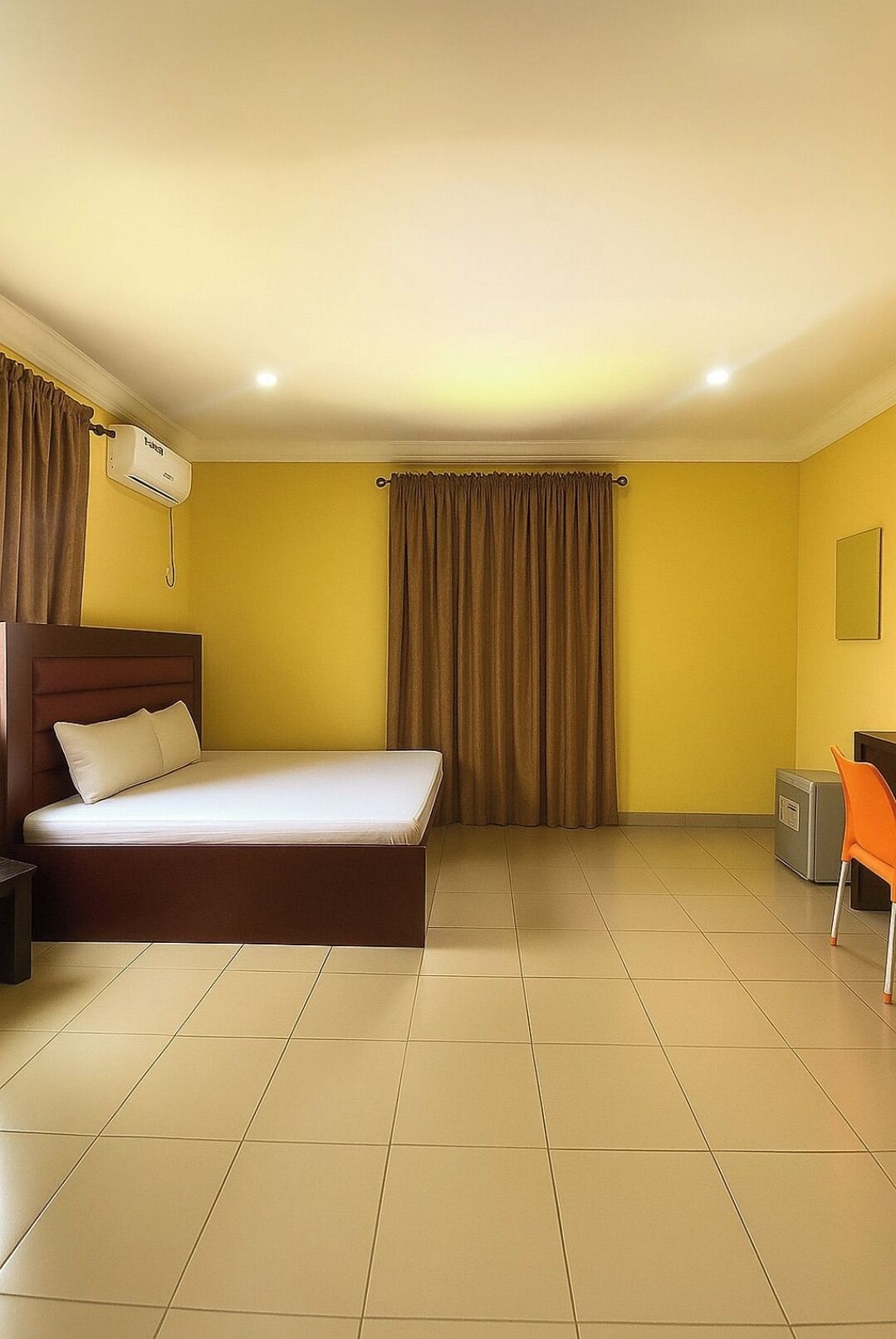 A hotel room with a bed, a desk, an air conditioning unit, and a chair.