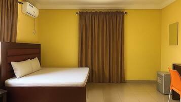 A hotel room with a bed, a desk, an air conditioning unit, and a chair.