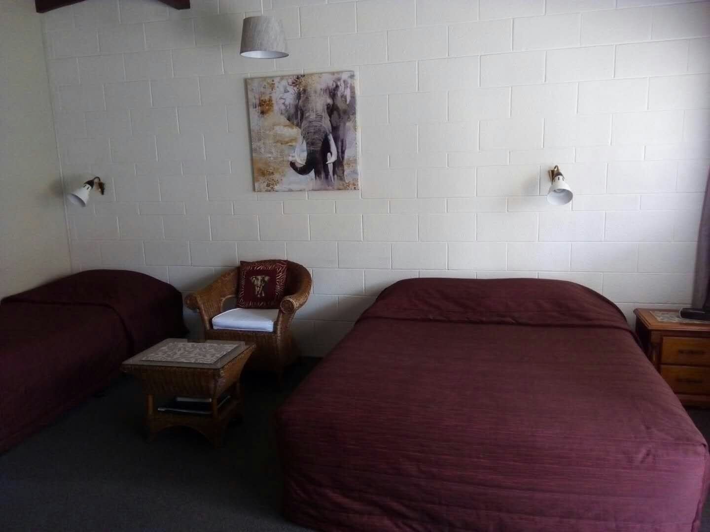 A room with two beds, a small wooden chair, a lamp, and a painting on the wall.