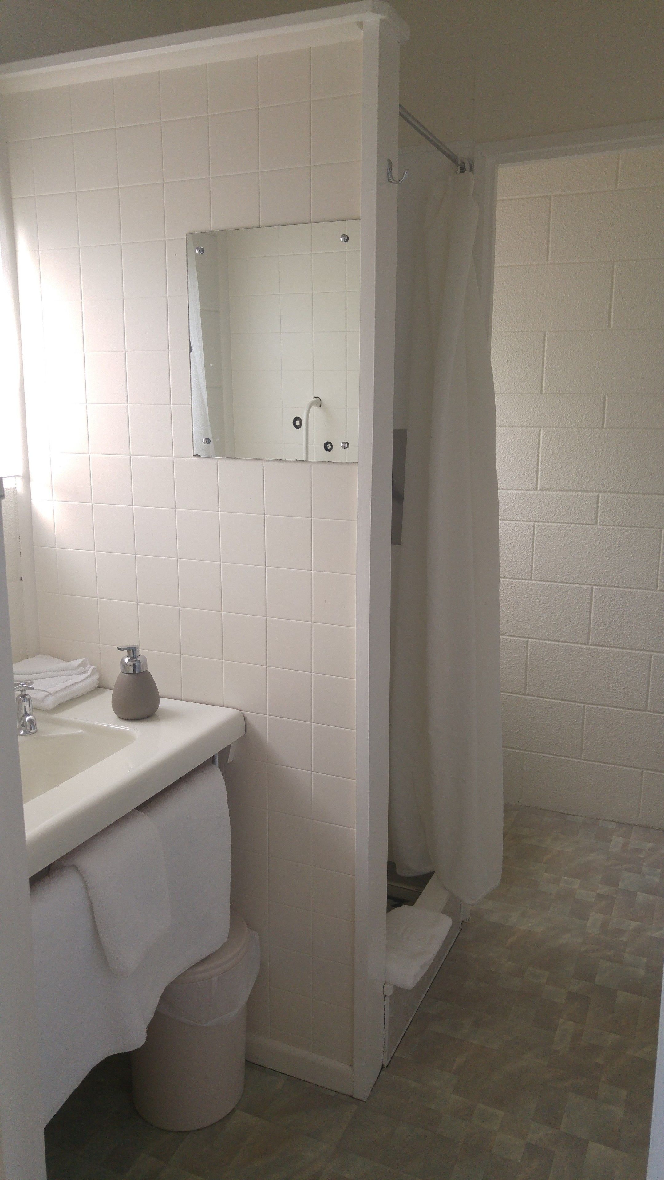 A bathroom with a white tiled wall, a sink with a mirror, a shower curtain, and a toilet.