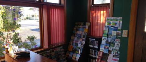 Una zona de recepción con mostrador de madera, un teléfono y un ventanal con cortinas rojas.