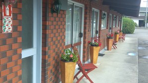 A brick building with a fire extinguisher sign, outdoor seating with red chairs, and potted plants. - Redwood Lodge Motel (Levin)