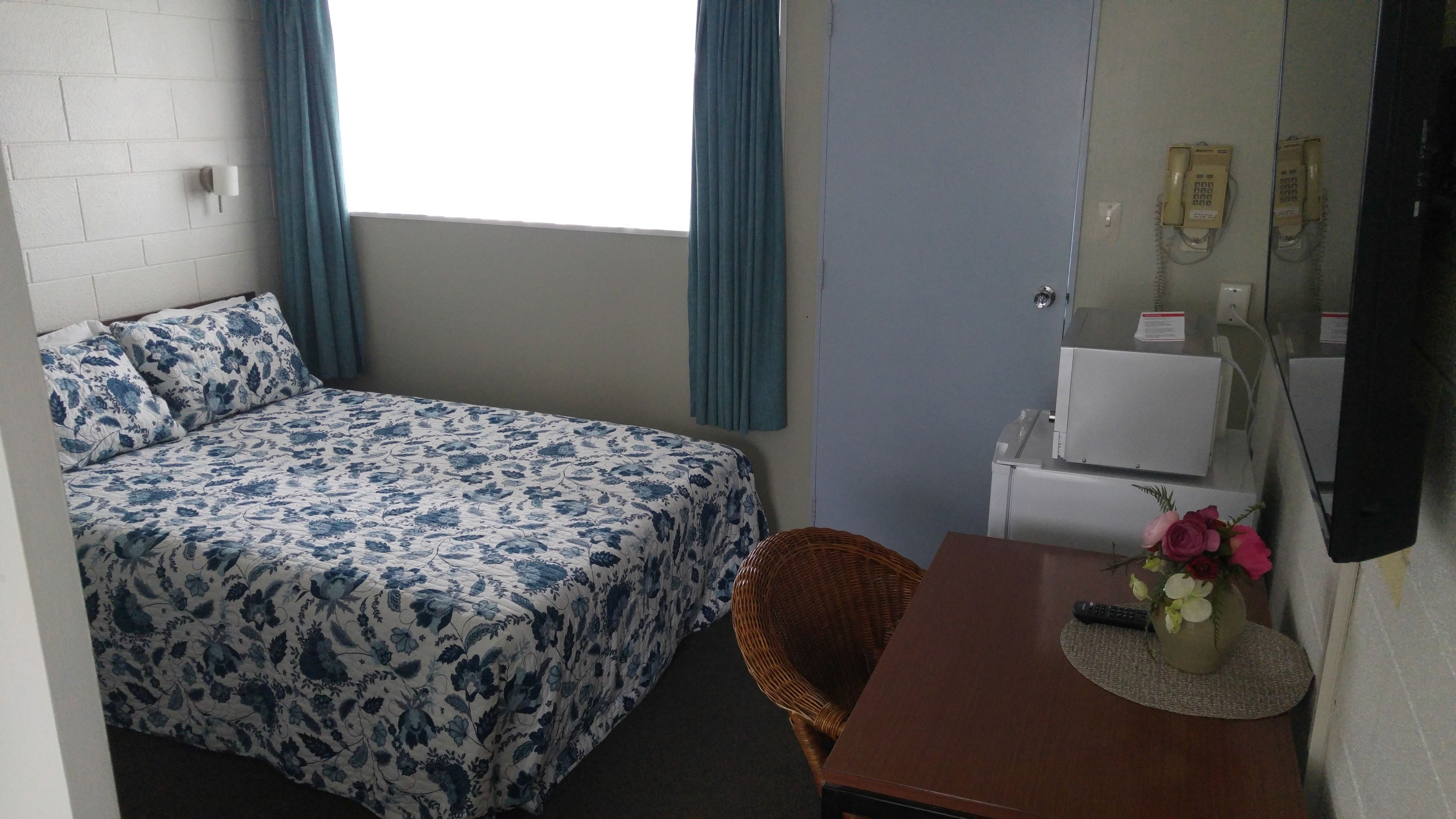 Een slaapkamer met een bed, een tafeltje met een bloemenvaas, een stoel, een bureau, een telefoon en een televisie.