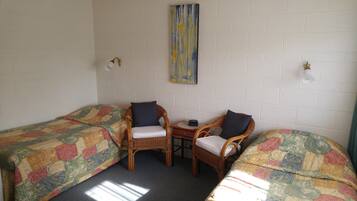 A room with two single beds, a small table, two wicker chairs, and a wall-mounted light fixture.