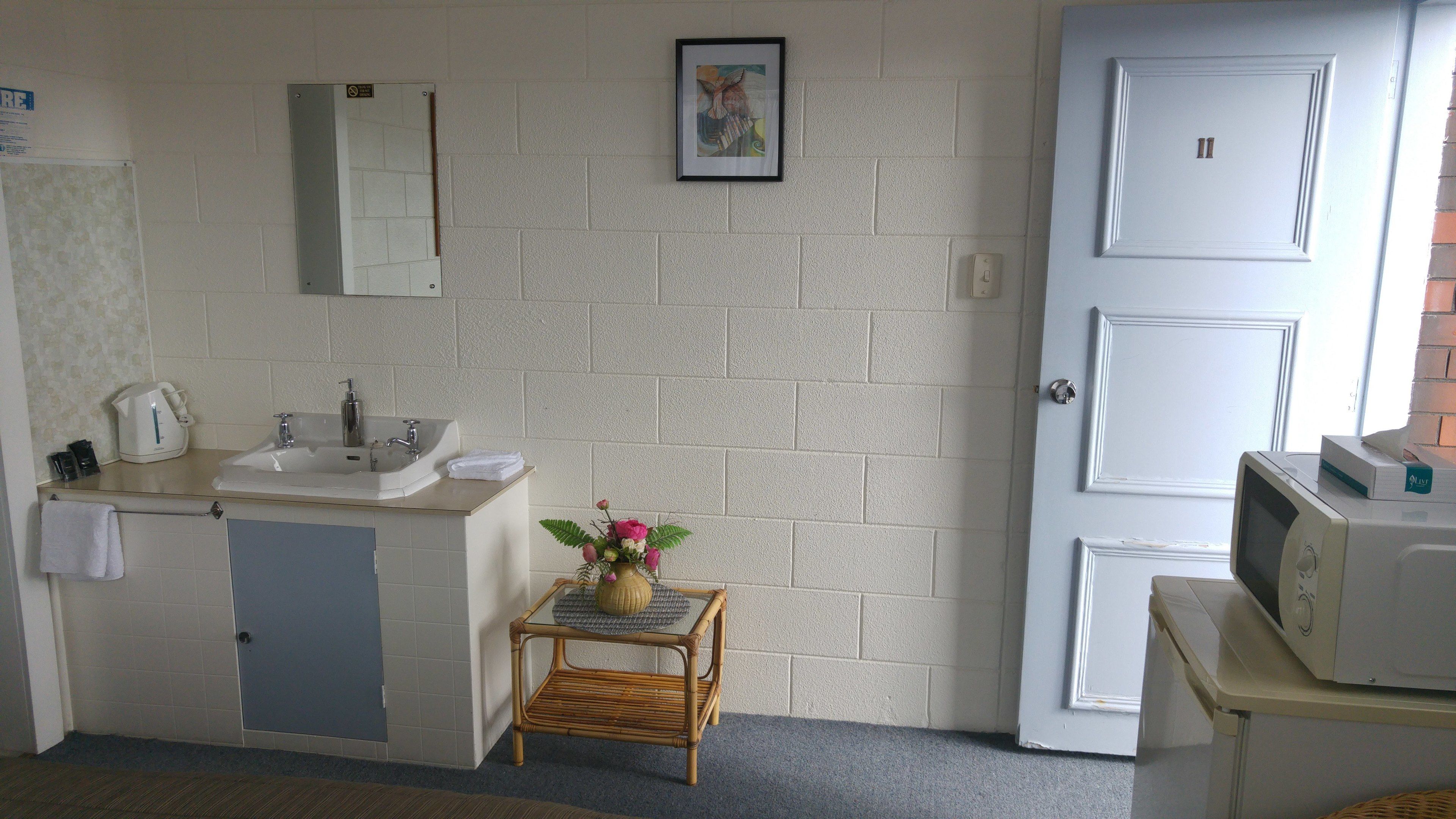 Un baño pequeño y limpio con un lavabo, espejo y una mesita con un florero.
