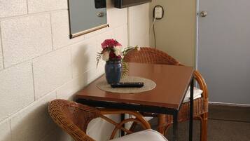 A room with a television mounted on the wall, a wicker chair, a small table with a vase of flowers, and a door.