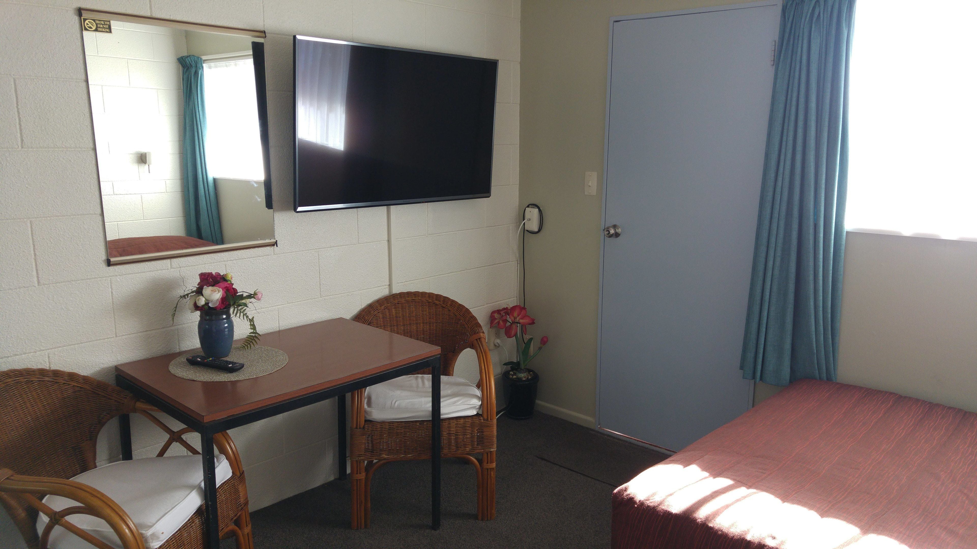 Una habitación con cama, una mesa y sillas, un televisor en la pared y una puerta.