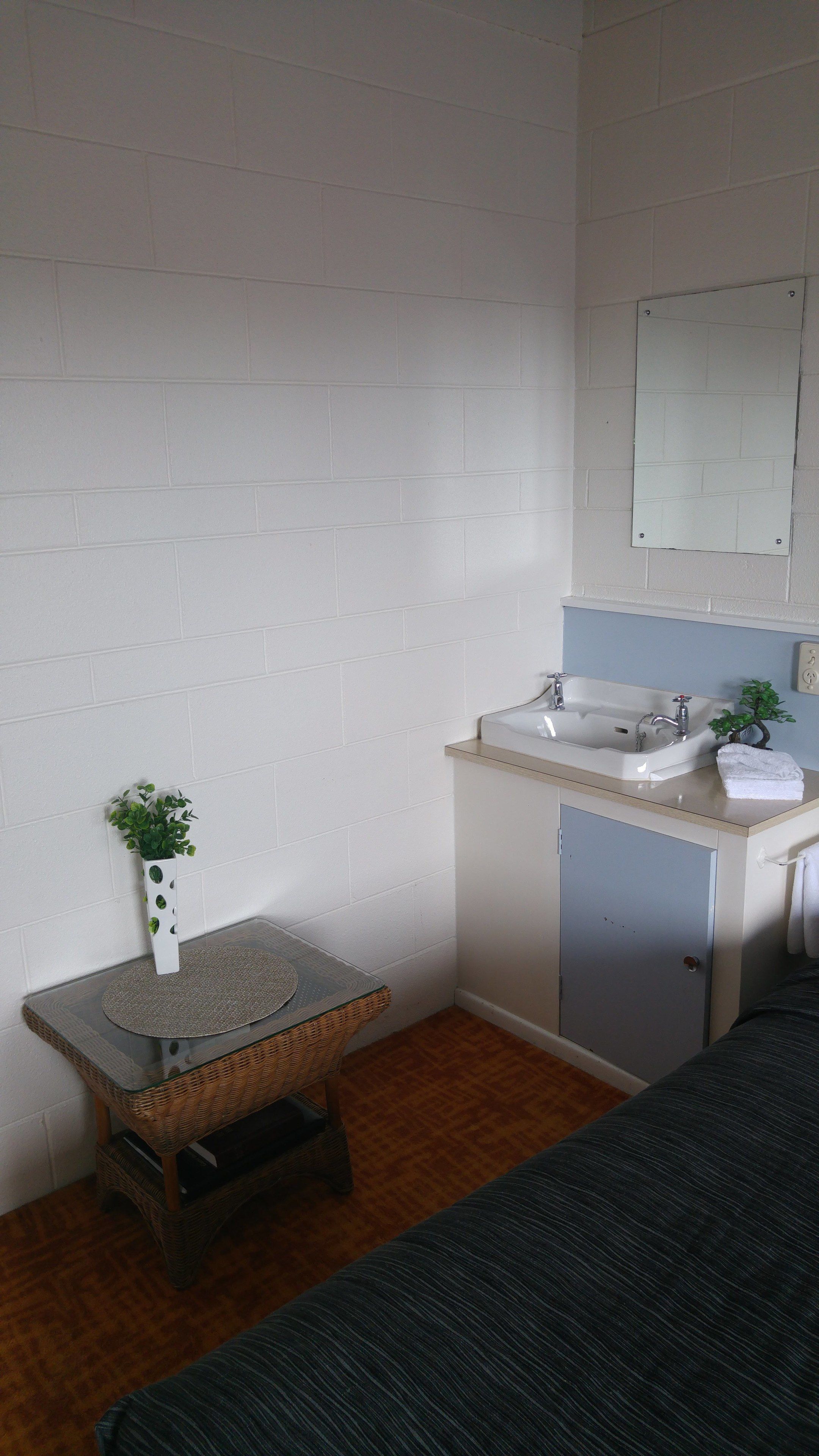 A small, clean bathroom with a white sink, a mirror, and a small potted plant on a glass table.