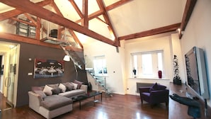 A spacious living area with a wooden ceiling, a staircase, a sofa, a coffee table, and a window. - Tsq Whitehall (London)