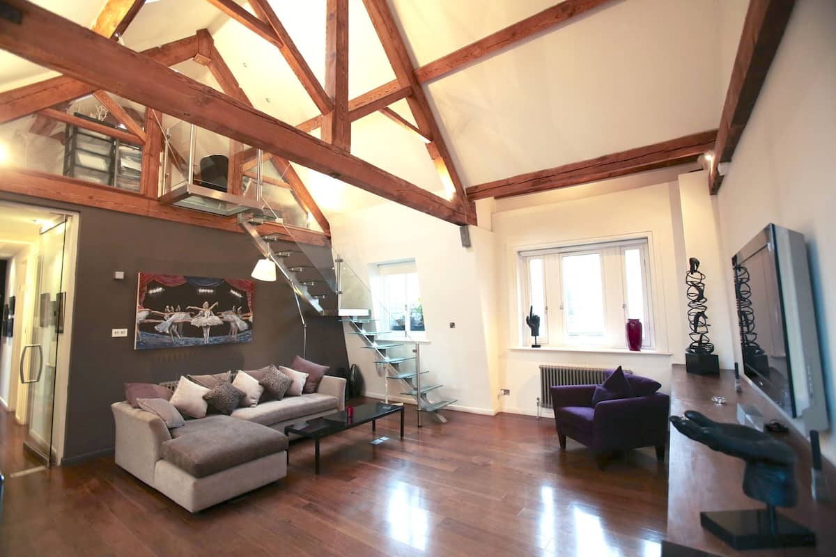 Un vaste espace de vie doté d’un plafond en bois, d’un escalier, d’un canapé, d’une table basse et d’une fenêtre.