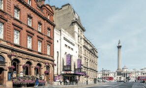 A street view with historic buildings, a prominent monument, and a red double-decker bus. - Tsq Whitehall (London)