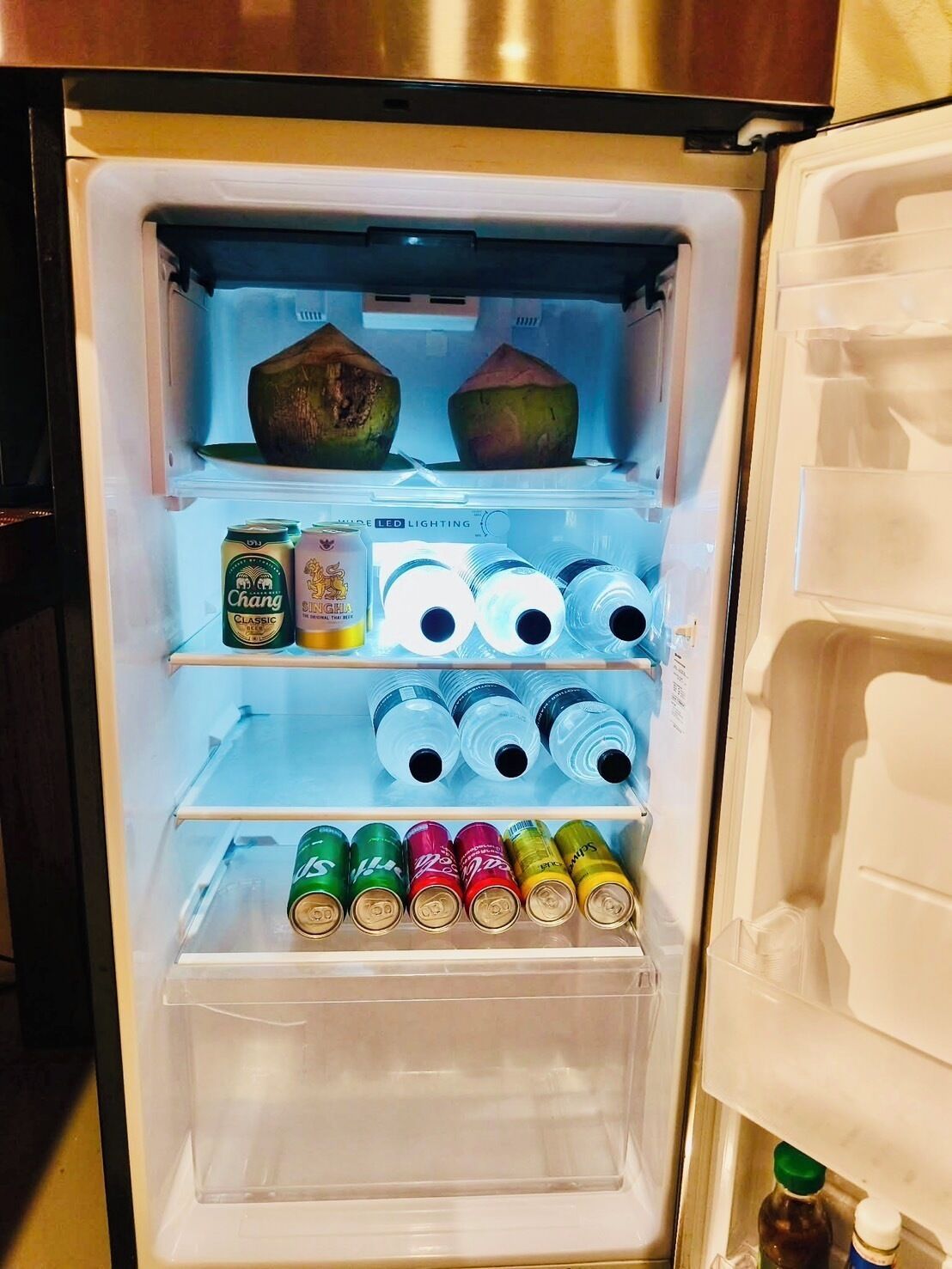 An open refrigerator with various beverages and a coconut.