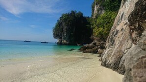 A beach with clear turquoise water, a rocky cliff, and boats in the distance. - Klong Muang Seaview (Krabi)