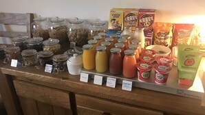 Una barra de desayuno con diversas opciones de alimentos y bebidas, como tarros de granola, cereales y zumos de frutas.
