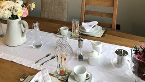 A dining table set with white tableware, a vase with flowers, and a large wall clock. - Lon Y Traeth Bed & Breakfast (Pentraeth)
