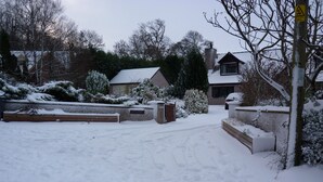 A snow-covered residential driveway leading to a house with a brick chimney and a visible garage. - Lon Y Traeth Bed & Breakfast (Pentraeth)
