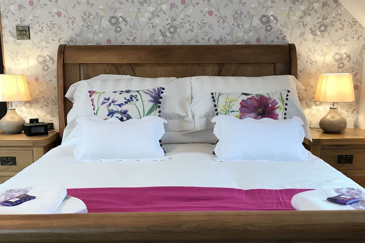 A neatly made bed with floral-patterned pillows, a wooden headboard, and a pink towel at the foot of the bed.