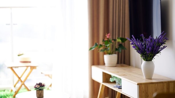 A modern living room with a wooden console table, a white vase with purple flowers, and a large flat-screen TV mounted on the wall. - Hometel Newlife Ha Long (Bai Chay)