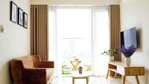 A modern living room with a sofa, a coffee table, a TV on a stand, and a balcony with curtains. - Hometel Newlife Ha Long (Bai Chay)