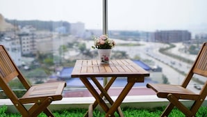 Two wooden chairs and a small table with a floral centerpiece on a balcony overlooking a cityscape. - Hometel Newlife Ha Long (Bai Chay)