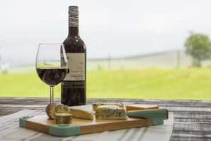 A bottle of wine, a glass of wine, and various cheeses on a wooden board. - The Living Collective (Hilton)