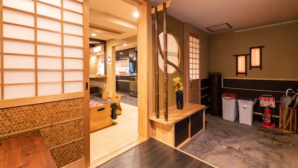 Um interior japonês tradicional com tatames, uma mesa de madeira baixa e uma porta deslizante que dá para uma área de cozinha.