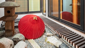 Um edifício japonês tradicional com um candeeiro de pedra, um guarda-sol vermelho e um caminho de madeira.