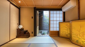 Un interior japonés tradicional con suelo de tatami, una puerta corrediza que da a un jardín y un shoji con diseños de plantas.