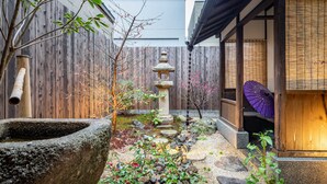 Perinteinen japanilainen puutarha, jossa on puinen aita, kivilyhty ja violetti aurinkovarjo.
