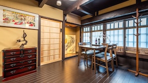 Een traditionele Japanse kamer met tatami vloeren, een lage tafel met stoelen, een houten kast met lades en een groot raam met uitzicht.